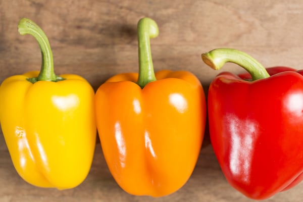 Selection of fresh red yellow and orange peppers on a wooden kitchen work surface